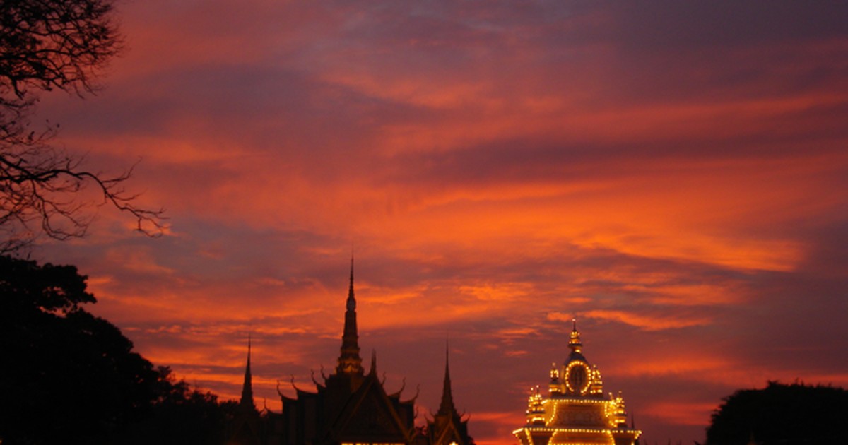 The Royal Palace in Phnom Penh, Cambodia, its spires and gate silhouetted and lit against a vivid orange sunset sky.